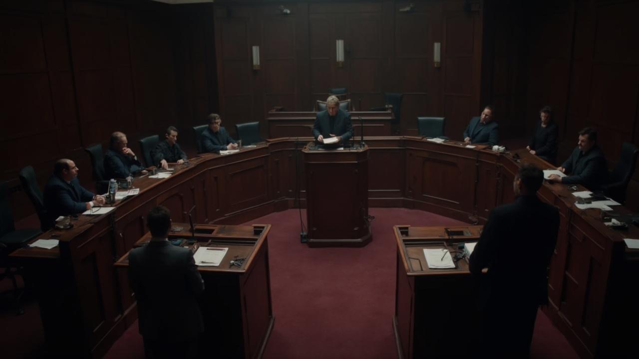Salle d'audience sombre avec des juges et avocats assis autour d'une table.